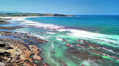 Kayalık uçurumlar ve turkuaz okyanus dalgalarının yer aldığı canlı bir plajın nefes kesici ve çarpıcı manzarasının tadını çıkarın.