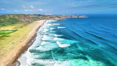 Güneşli ve sıcak bir günde el değmemiş bir plajı ve yumuşak dalgaları gösteren nefes kesici bir hava görüntüsü.