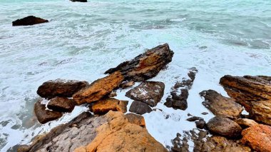 Çarpıcı kayalık sahil şeridinde taşlara çarpan turkuaz dalgalar var, doğa fotoğraflarını çekmek için mükemmel.