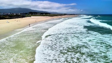 Bu plaj dalgaların, güneşli gökyüzünün ve güzel sahil şeridinin tadını çıkaran insanların nefes kesici manzarasını sunuyor.