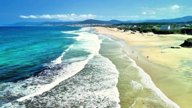 Göz kamaştırıcı hava görüntüleri, berrak mavi gökyüzünün altında hafif dalgaların yer aldığı pitoresk bir sahili güzel bir şekilde gösteriyor.