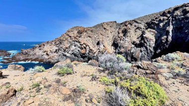 Berrak mavi gökyüzünün altındaki sakin okyanus sularının yanında engebeli uçurumların nefes kesici ve büyüleyici bir manzarası var.