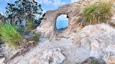 Güzel bir kıyı kaya oluşumunun, canlı, renkli bir gökyüzünün altında sakin bir deniz manzarasını çerçeveleyen kemeri vardır.