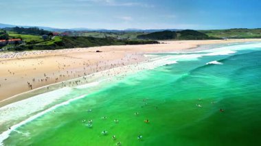 Kristal gibi berrak yeşil suları olan güzel bir sahil manzarası ve insanların eğlendiği canlı kumlu bir sahil.