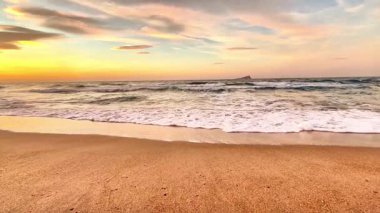 Şaşırtıcı derecede güzel bir gün batımı okyanus dalgalarını aydınlatıyor. Yakınlardaki kumlu kıyı şeridine hafifçe vuruyor.