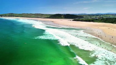 Çarpıcı hava görüntüleri, canlı bir sahil sahnesini, sörfçülerle ve berrak turkuaz sularla güzel bir şekilde gösteriyor.