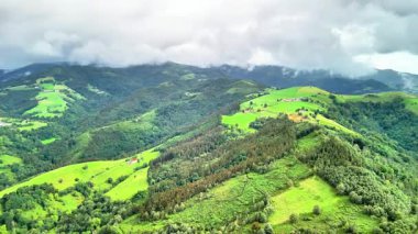 Canlı yeşil tepeler ve görkemli dağlar bulutlu bir gökyüzünün altında gururla duruyor.