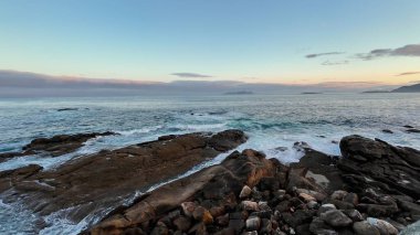 Alacakaranlıkta sakin bir okyanusun nefes kesici manzarası, dalgaların kayalık kıyı şeridine çarpması..