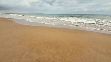 Yumuşak kumları ve bulutlu gökyüzünün altında süzülen yumuşak dalgaları olan sakin bir sahil hayal edin.