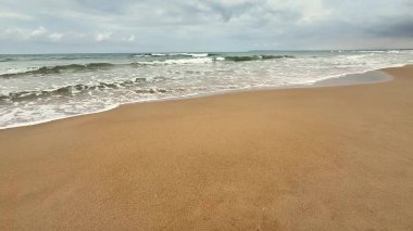 Huzurlu ve sakin bir sahil sahnesi. Yumuşak dalgaların kasvetli bir gökyüzünün altında yumuşak kumu yaladığı.