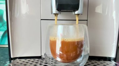 Şık ve modern bir espresso makinesi ustalıkla temiz bir bardağa lezzetli bir fincan kahve dolduruyor.