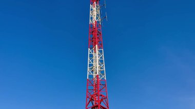 Belirgin kırmızı ve beyaz bölümleri olan yüksek bir iletişim kulesi, açık mavi gökyüzüne güzelce yerleştirilmiş.