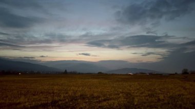 Anımsatıcı ve pitoresk bir alacakaranlık sahnesi geniş kırsal bir alanda yavaşça yuvarlanan tepeleri gösteriyor.