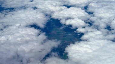 Nefes kesici bir hava perspektifi, yukarıdaki yumuşak, kabarık bulutların arasından süzülen canlı yeşillik gölgeleri sergiliyor.