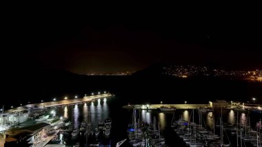 Geceleri göz kamaştırıcı bir yat limanı, aydınlatılmış tekne ve rıhtımları resimli bir dağ zeminiyle aydınlatıyor.