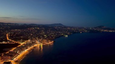 Alacakaranlıkta parlayan ışıklarla aydınlatılmış güzel bir sahil şehrinin nefes kesici ve çarpıcı manzarası.