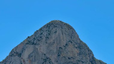 Kayalık bir dağın nefes kesici manzarası yukarıdaki parlak ve berrak mavi gökyüzüne karşı güzel bir şekilde yükseliyor.