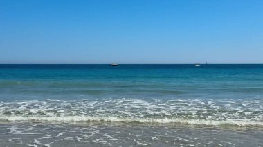 Yumuşak dalgaları ve açık mavi gökyüzü olan sakin bir sahil. Yaz atmosferi ve güneşi emmek için ideal.