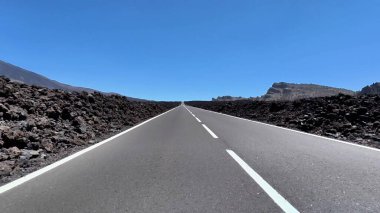 Nefis bir asfalt yol güzel bir şekilde uzanıyor, el değmemiş mavi gökyüzünün altında eşsiz volkanik kayalarla çevrelenmiş.