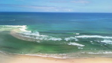 Sakin sahil dalgalarının ve berrak, güneşli bir gökyüzünün altındaki canlı mavi suların nefes kesici manzarasını hissedin.