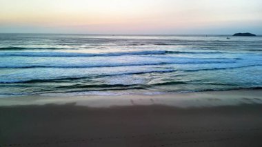 Okyanus dalgalarının sakinliğinin tadını çıkarmak için bir dakikanızı ayırın. Huzurlu bir kumsalda, çarpıcı bir alaca karanlık gökyüzünde hafifçe sarmaş dolaş.