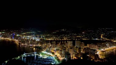 Alacakaranlıktaki kıyı şehrinin parlak ve renkli ışıklarını güzel bir şekilde gösteren nefes kesici bir gece manzarası.