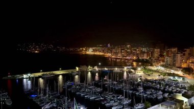 Göz kamaştırıcı şehir ışıklarının su yüzeyine yansıdığı büyüleyici bir liman sahnesi.