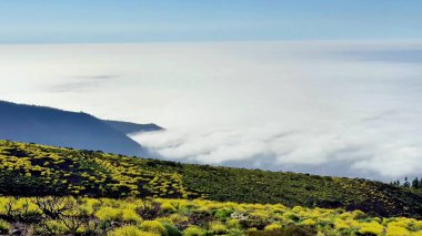 Nefes kesen dağ manzarası, üzerinde çarpıcı bir bulut örtüsüyle tamamlanmış canlı bir bitki örtüsüyle süslenir.