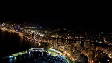 Nefes kesen bir hava manzarası, gece aydınlanan canlı ve canlı bir kıyı şehrini güzel bir şekilde gösteriyor.