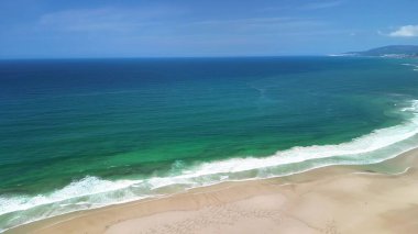 Yumuşak okyanus dalgaları ve yumuşak kumlu kumsalın berrak mavi gökyüzünün altında kendini sakinleştirici güzelliğe daldır.