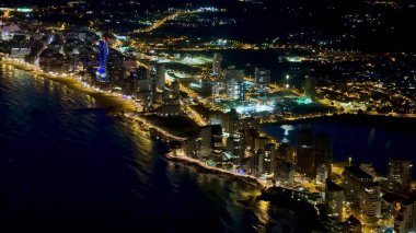 Kıyı kenti kıyı şeridi boyunca renkli ışıklarla parıldayan nefes kesici gece hava manzarası.