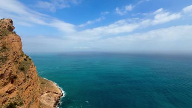 Çarpıcı bir manzara, canlı mavi bir okyanusa bakan yüksek bir uçurumdan nefes kesici bir kıyı manzarası sunar.