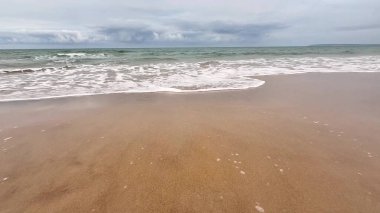Nazik dalgaların güzel sakin manzarası bulutlu gökyüzünün altındaki altın kumlu kumsalda durmadan süzülüyor.