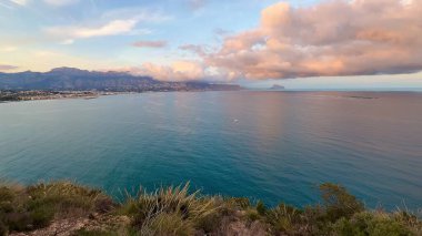 Nefes kesici bir kıyı manzarası serin, sakin sular ve çarpıcı bir günbatımında renkli bulutlar sunar.