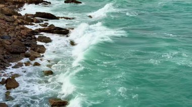 Kıyı dalgalarının dingin ve sakin güzelliğini keşfedin. Ritmik olarak kayalık oluşumlara çarpar.