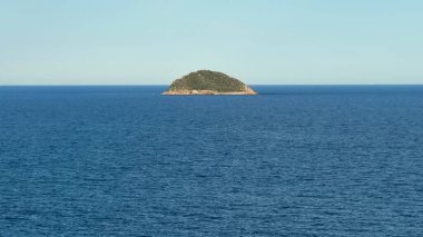 Sakin ve sakin bir ada, parlak ve berrak bir gökyüzünün altında, derin mavi denizle zarifçe çevrilidir.