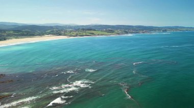 Nefes kesici bir hava fotoğrafı, berrak mavi okyanusu ve berrak gökyüzünün altındaki gür, canlı kıyı şeridini yakalar.