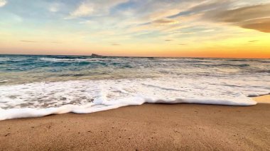 Nazik dalgaların sakin bir sahnesiyle baş döndürücü ve renkli bir günbatımında altın sahili hafifçe okşayarak