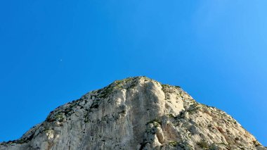 Engebeli, kayalık bir dağın nefes kesici manzarası görkemli, parlak, mavi gökyüzüne karşı duruyor.