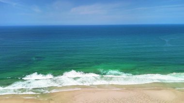 Nefis, sakin bir sahil sahnesi sergileniyor çarpıcı turkuaz sular ve berrak mavi gökyüzünün altında yumuşak, yumuşak dalgalar.