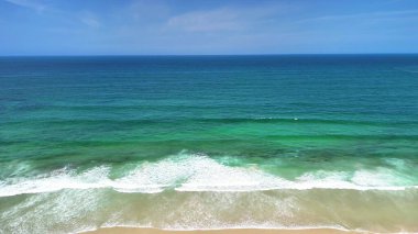 Canlı turkuaz suları ve hafif dalgaları kıyıya vuran sakin bir sahilin büyüleyici hava manzarası..