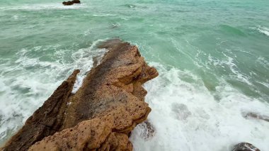 Dalgalar kayalık çıkıntılara çarpar ve sakin bir sahil manzarası yaratır. Doğa meraklıları için mükemmel..