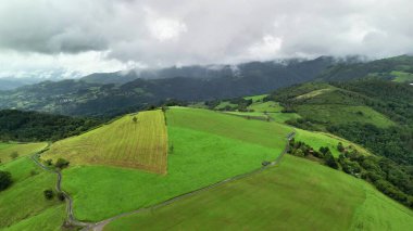 Göz kamaştırıcı drone görüntüleri bulutlu bir gökyüzünün altındaki canlı yeşil tarlaları ve görkemli dağları güzel bir şekilde gösteriyor.