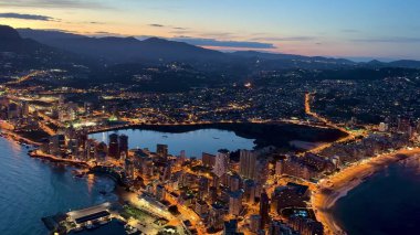 Canlı bir şehir manzarası ve alacakaranlıkta çarpıcı bir kıyı şeridi manzarayı güzellikle aydınlatıyor.