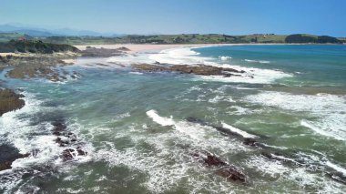 Güzel bir kayalık sahil şeridinin ve berrak mavi gökyüzünün altındaki sakin plajın nefes kesici insansız hava aracı görüntüleri..