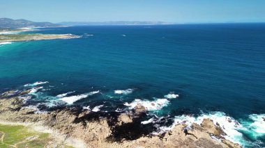 Sersemletici bir hava manzarası sakin bir kıyı şeridi sergiliyor, berrak turkuaz sular ve engebeli kayalık kayalıklar var.