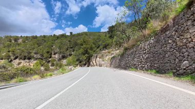 Güzel, dolambaçlı bir yol, parçalı bulutlu bir gökyüzünün altında yeşil ve kayalık duvarlarla çevrilidir.