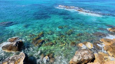 Kristal berraklığında, canlı mercan resifleri ve kıyı kayalarını gösteren okyanusun nefes kesici manzarasını deneyimleyin.