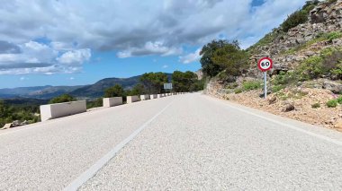 Bereketli yeşillik ve canlı gökyüzü ile çevrili pitoresk bir dağ yolu, seyahat görüntüleri için mükemmel..