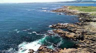 Nefis bir kıyı manzarası güzel bir şekilde sergilenen engebeli kayalar ve berrak bir gökyüzünün altındaki canlı turkuaz deniz.